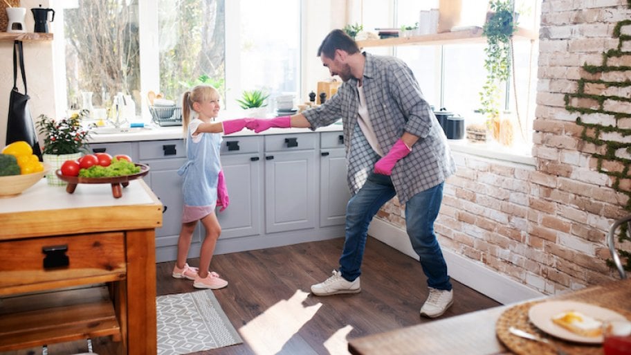 daughter and father fist bump with pink gloves and smile as they prepare to clean the kitchen