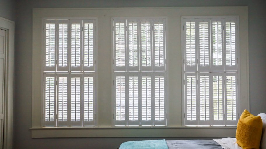 Three large windows with estate shutters in a bedroom