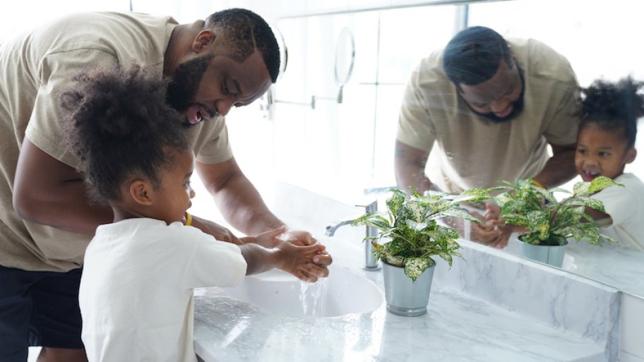 father helping his young daughter was her hands in sink with marble countertop