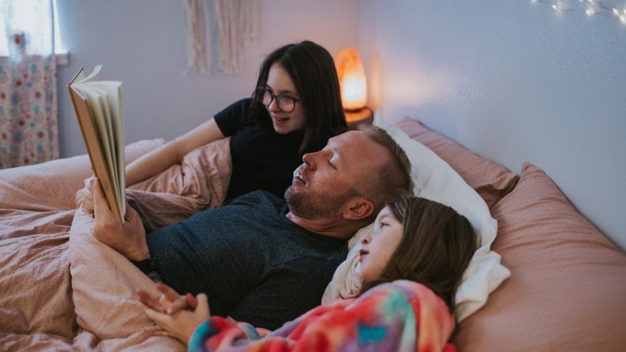 A father reading a book to his daughters in bed
