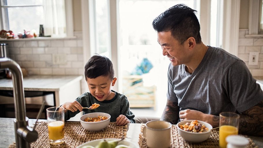 Father and son eat breakfast in kitchen