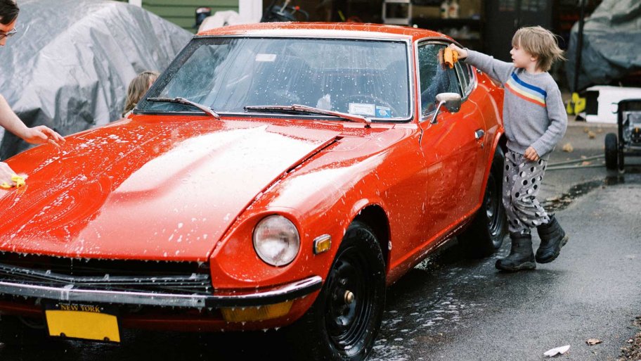 A little boy with his father wash their red vintage car in the driveway of their home