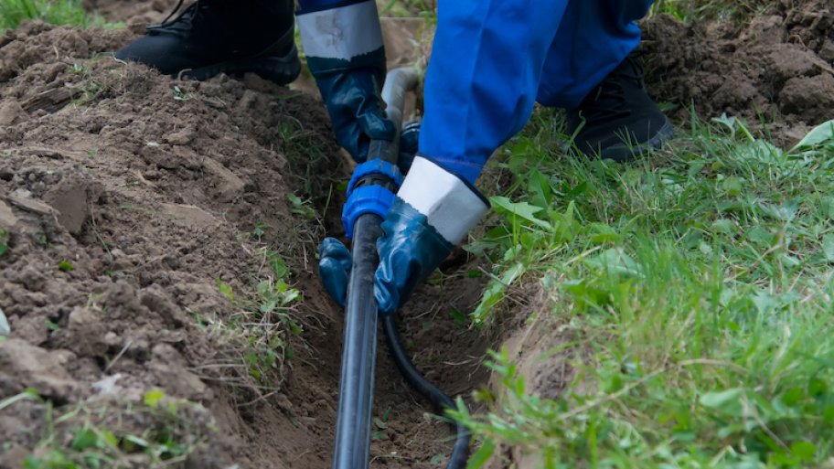 hands of the worker, in blue gloves, laid a plastic pipeline in an open trench in the ground