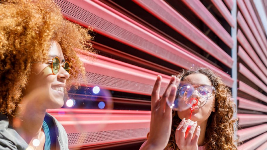 Female friends playing with bubbles in front of a corrugated fence