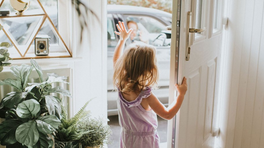 A girl waving out the front door on a summer day