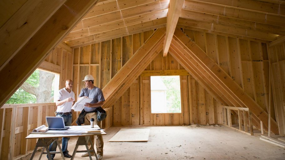 Home builders discuss plans in attic of framed house