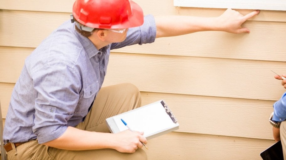 home inspector with pen and paper, pointing at wall