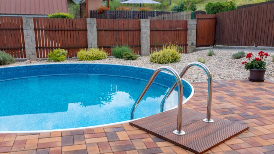 small round home swimming pool with silver stairs and brick patio