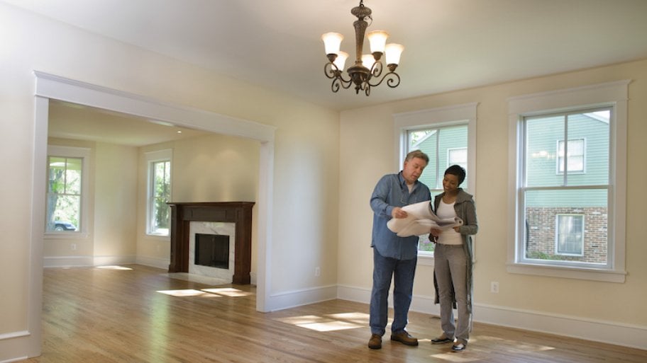 a homeowner and contractor look at renovation plans in an empty house