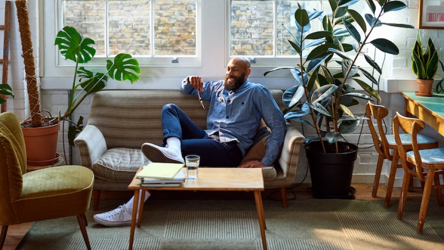 man sits on couch in living room next to rubber tree plant.
