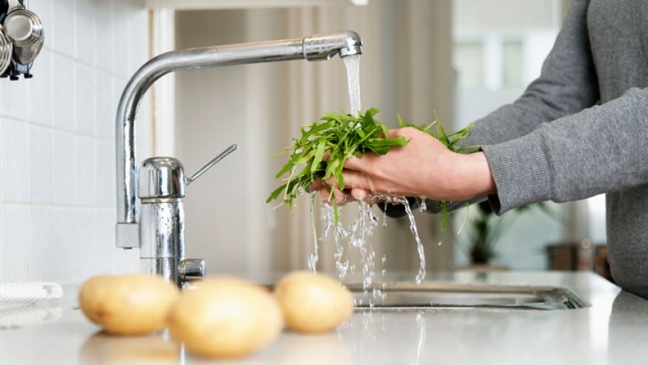 man washing greens in kitchen sink