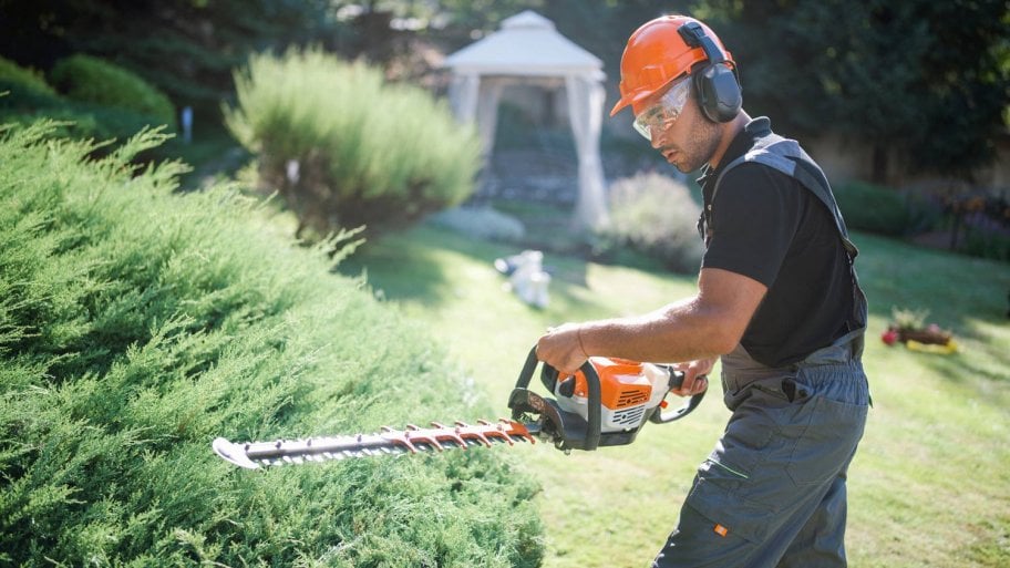 A landscaper trimming hedge with a power saw