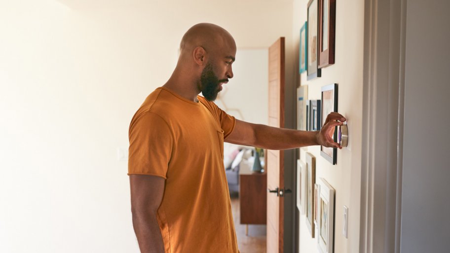 A young man adjusting the temperature of his home using a thermostat