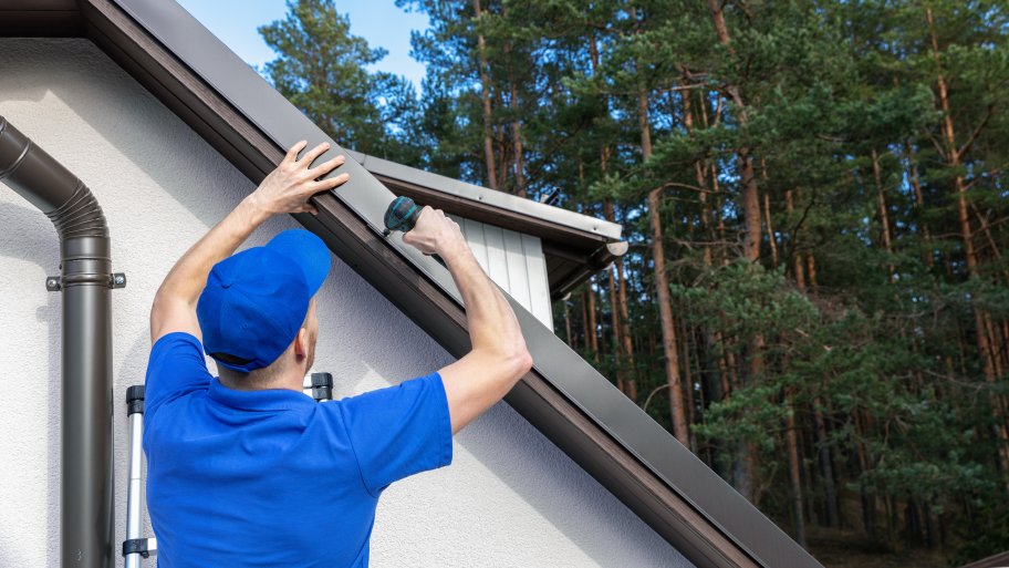 A roofer installing a metal drip edge along the side of a roof