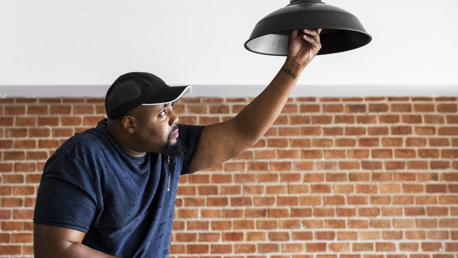 Man stands on lander and replaces bulb in ceiling light (Photo by Rawpixel.com - stock.adobe.com)
