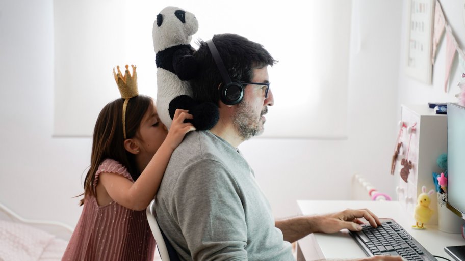 A man working on his computer with his daughter playing behind him