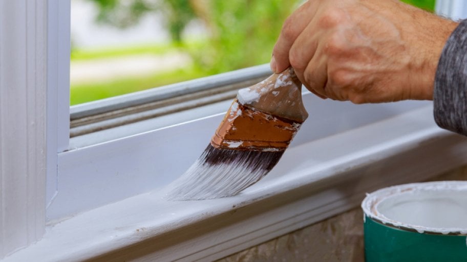 Man’s hand painting window trim white