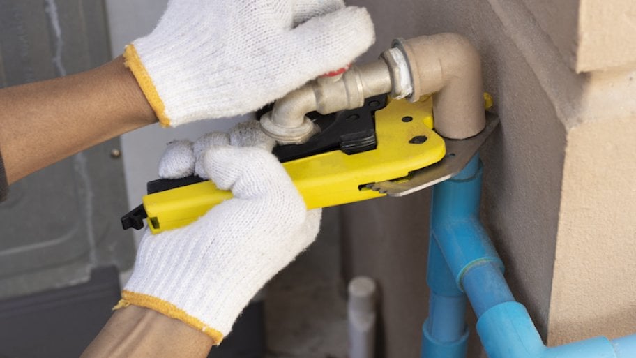 gloved hands holding pipe cutter against pipe