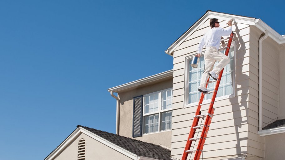 A professional standing on a ladder paints the exterior of a house