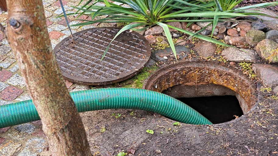 Septic tank with an open cover and green hose for pumping Septic tank with an open cover and green hose for pumping