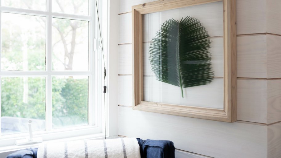 Shiplap accent wall with framed palm leaf next to open window and navy chair