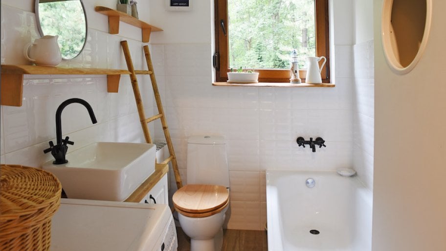 shot of small bathroom with white tile, white sink, bathtub and toilet, and tan accents