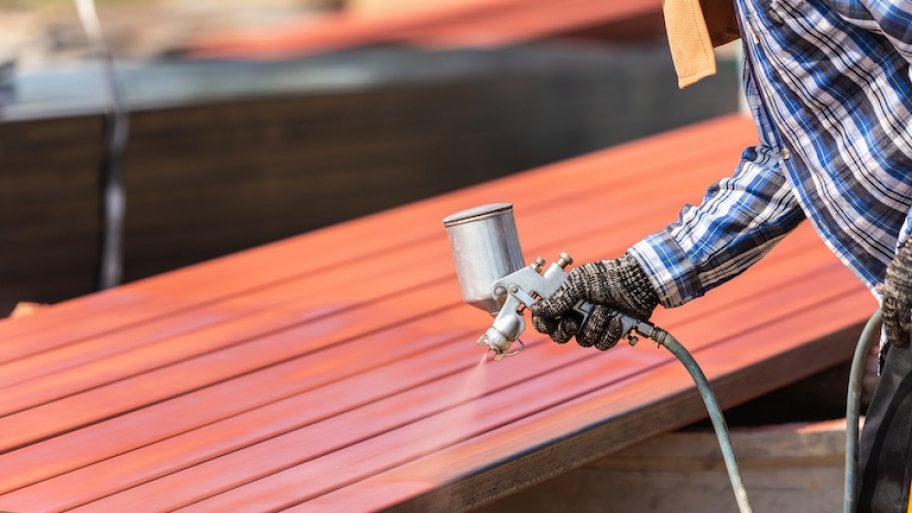 Worker spraying paint to steel pipe