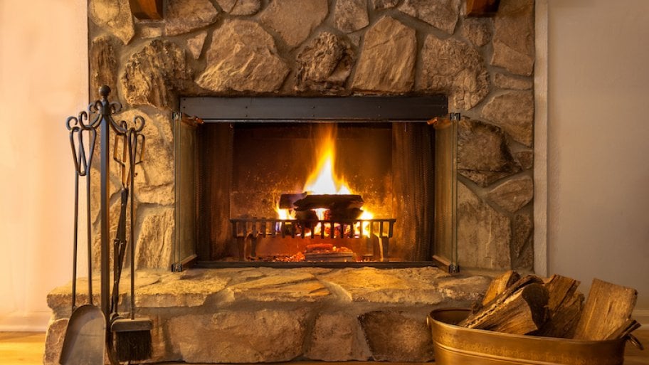 a stone fireplace with wood and fire with a bucket of firewood to the right