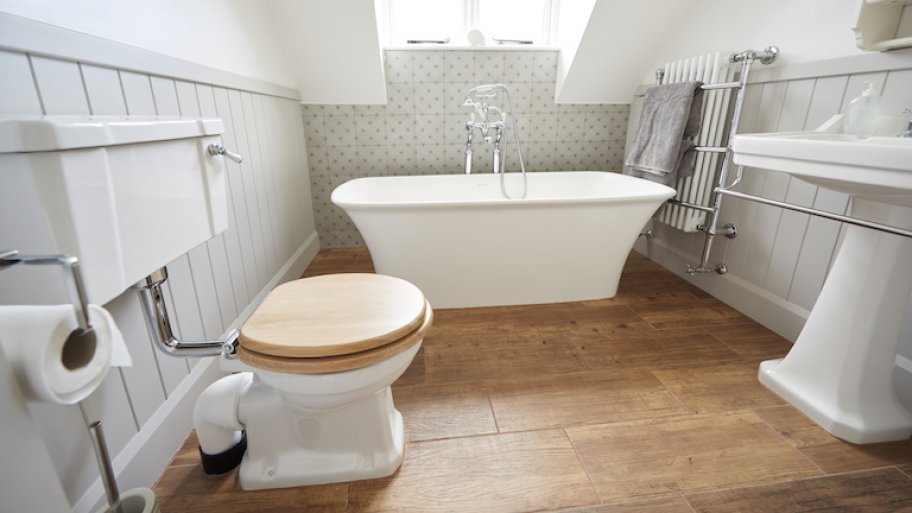 bathroom with white walls and fixtures and medium wood toned vinyl flooring