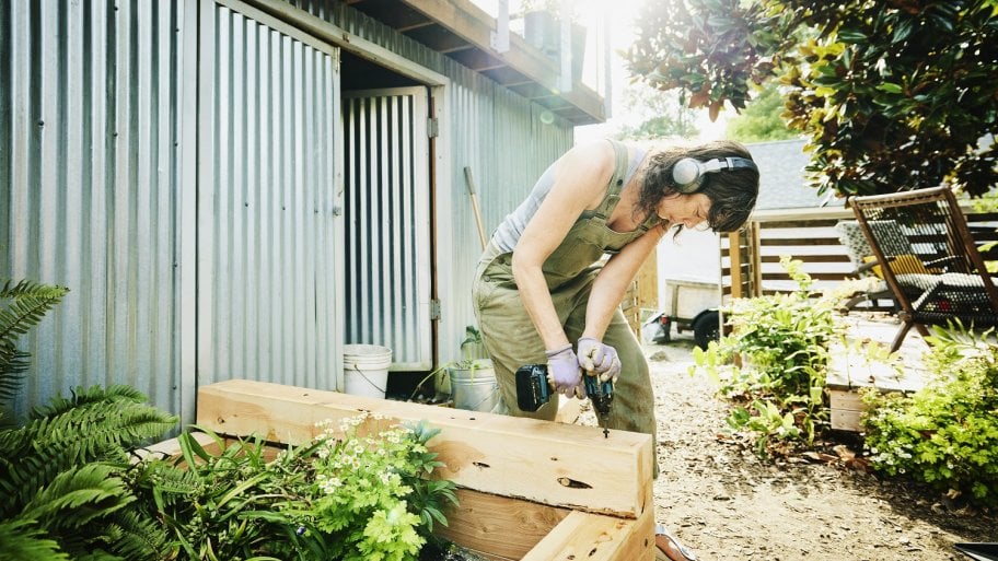 Woman building raised garden beds in backyard on summer afternoon