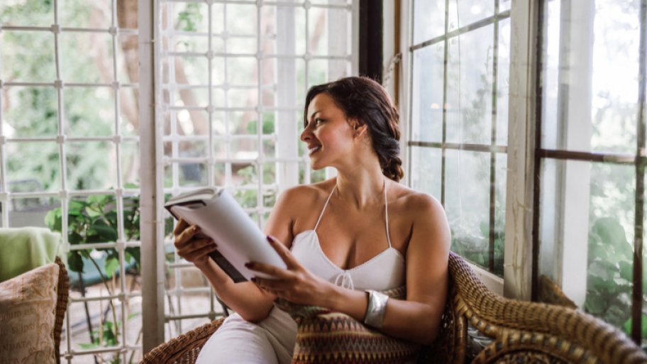 Woman reading book in sunroom and smiling