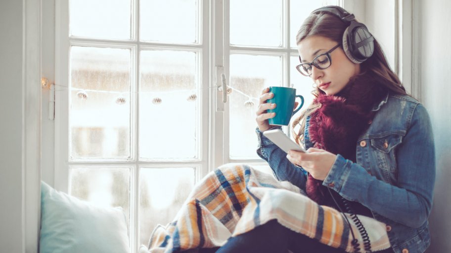 A young woman sitting by the window listening to music