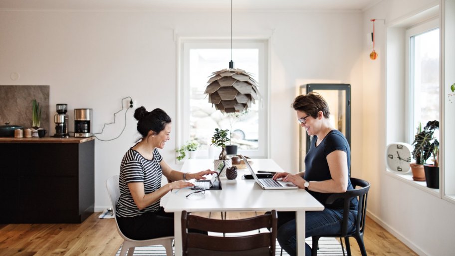 Two women working on their laptop at their living room table
