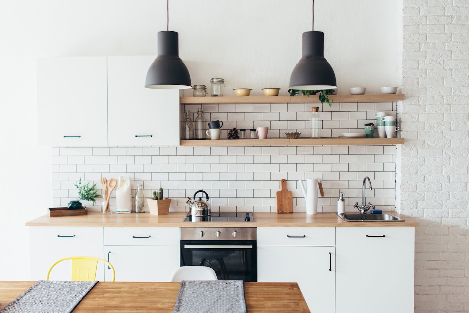 Modern kitchen with white subway tile backsplash, white cabinets, wood open shelves and black pendant lights