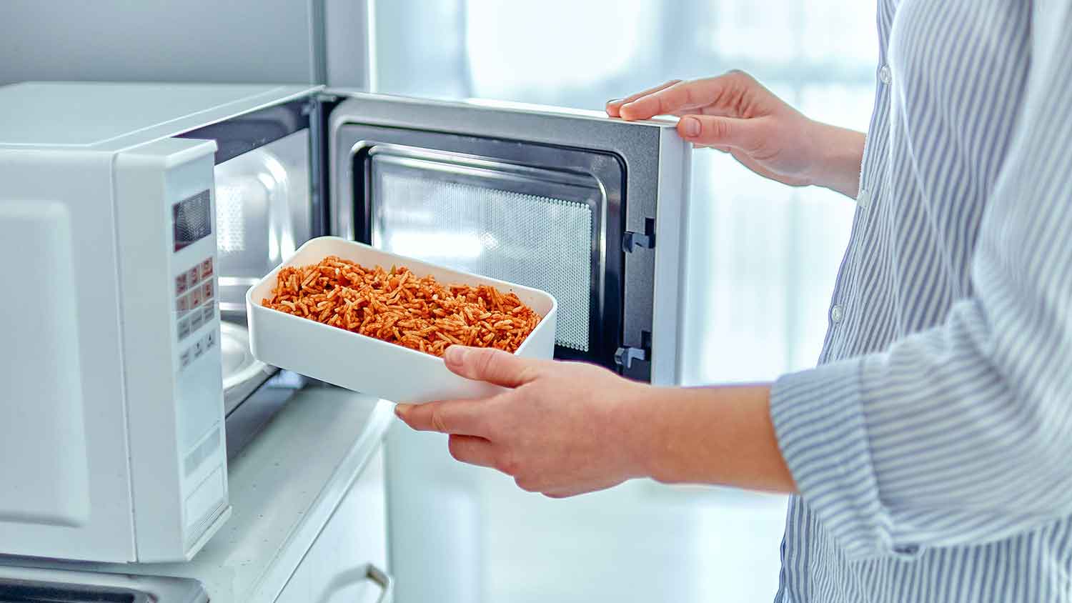 Woman taking a plate with food out of the microwave