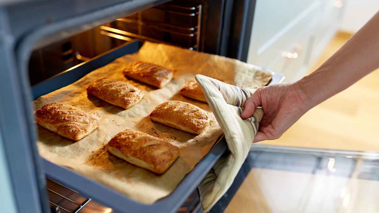 A person taking a tray of baked goods out of the oven.