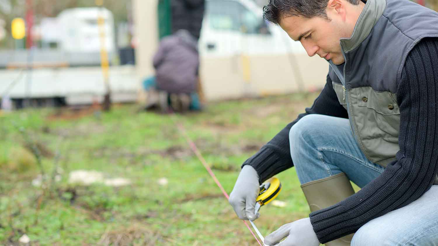 Handyperson using a measuring tape to calculate the yard area