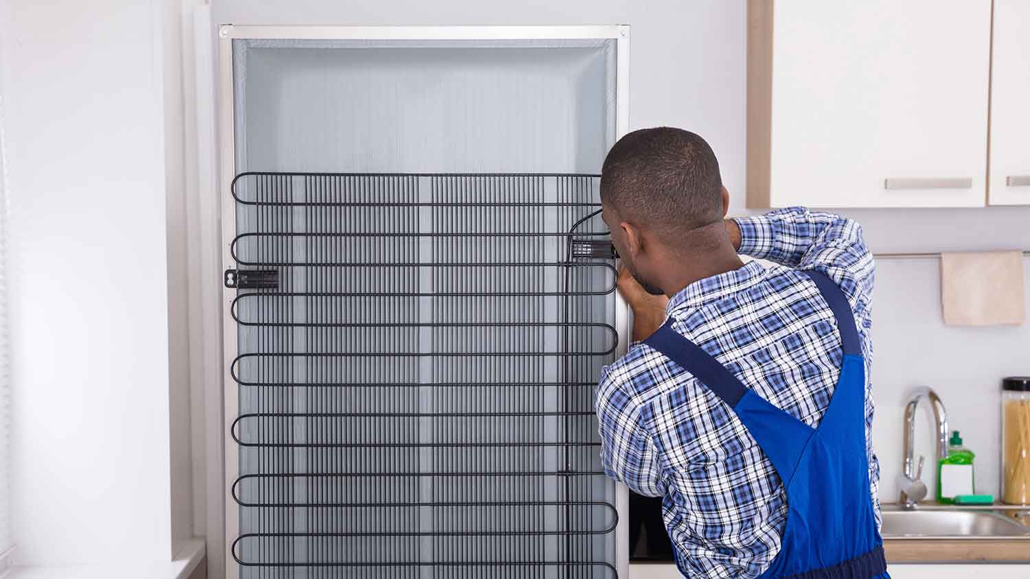Technician in the kitchen inspecting refrigerator coils