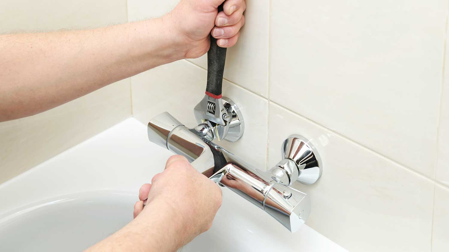 Plumber using wrench to tighten a tub faucet 