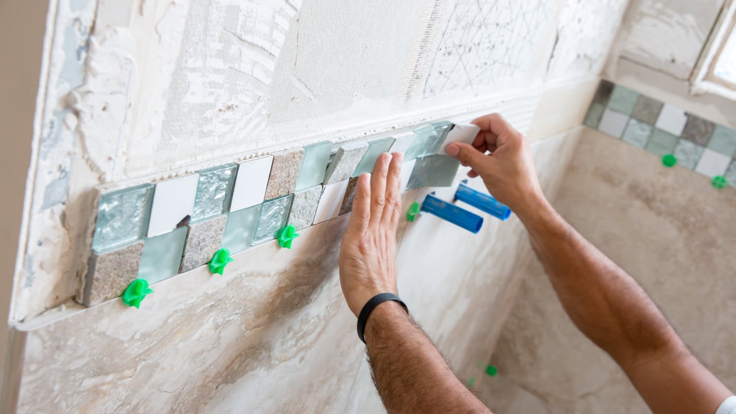 A professional installing a tiled border for the shower wall