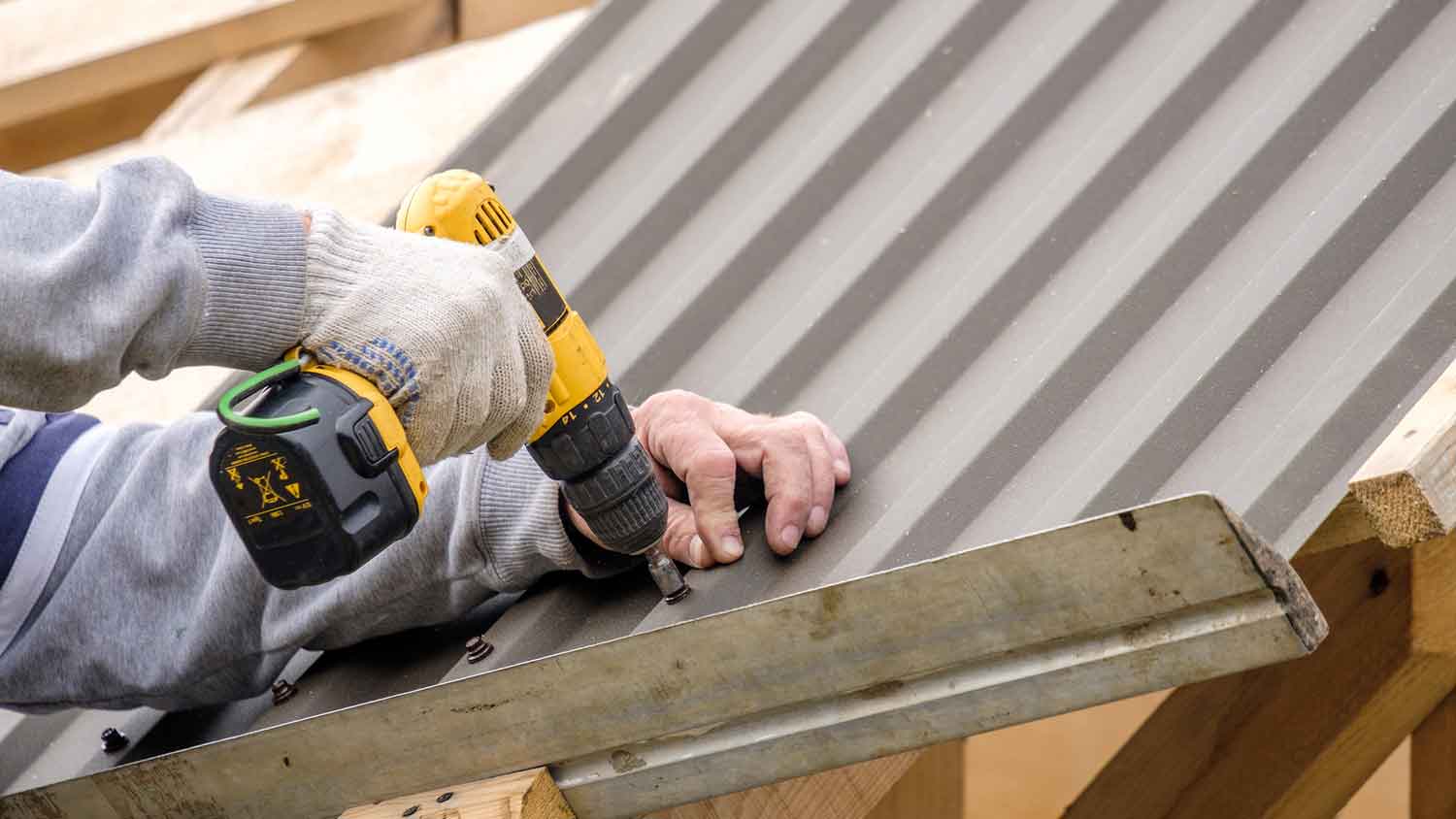 Roof professional using screwdriver to install tin roof