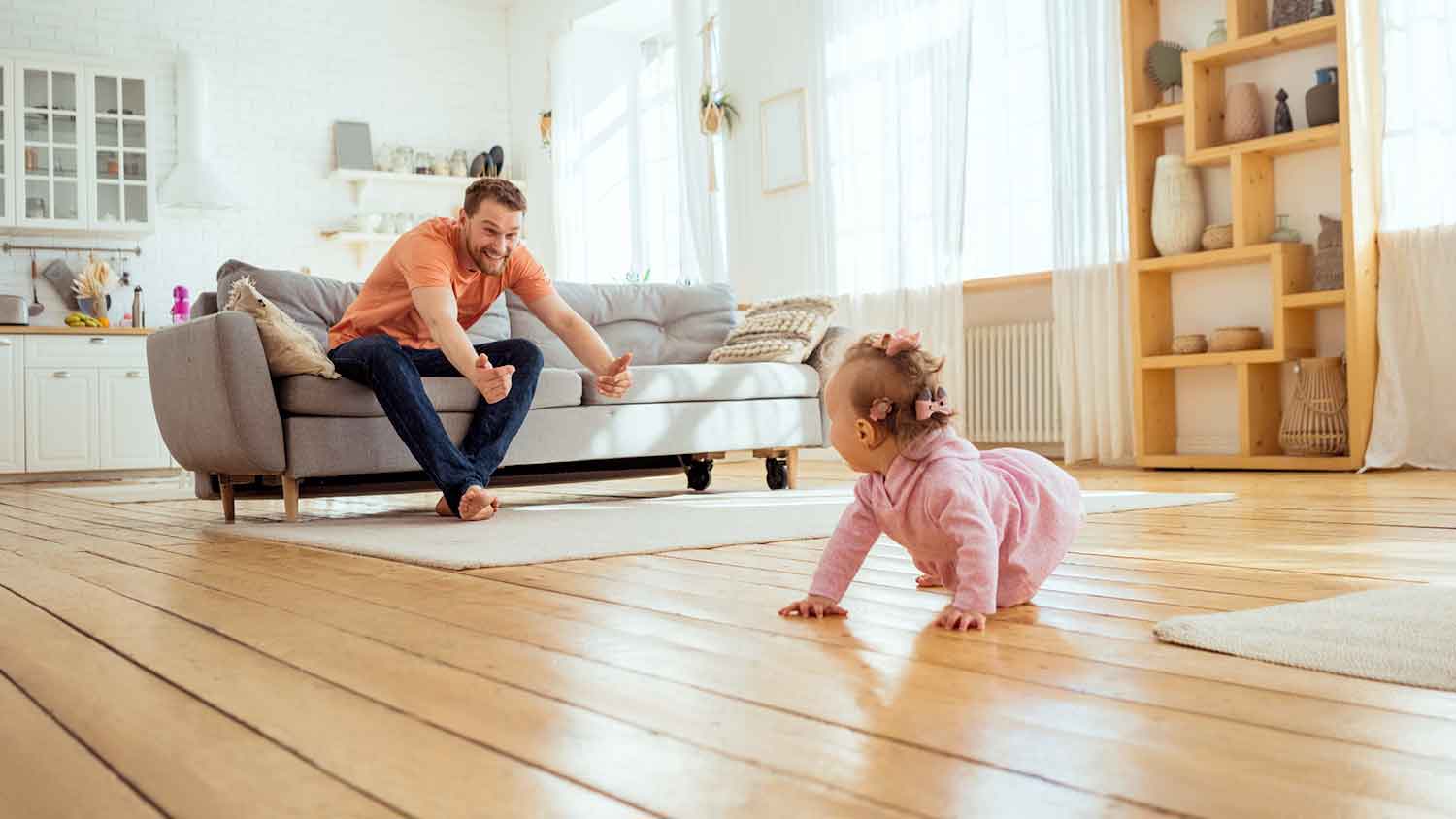 Father watching daughter crawling on hardwood flooring