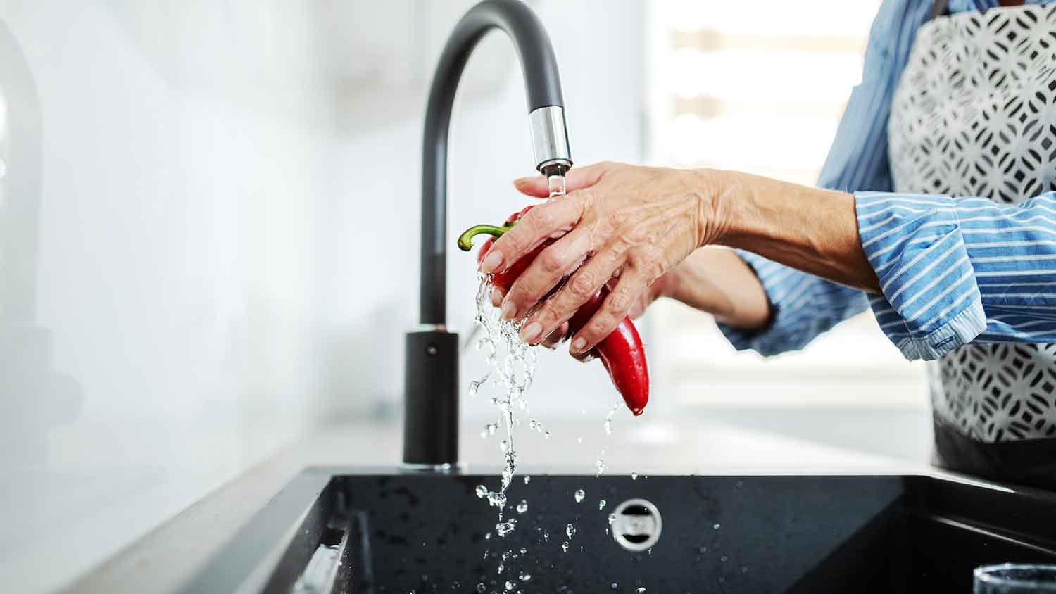 Woman washing a red pepper in the sink