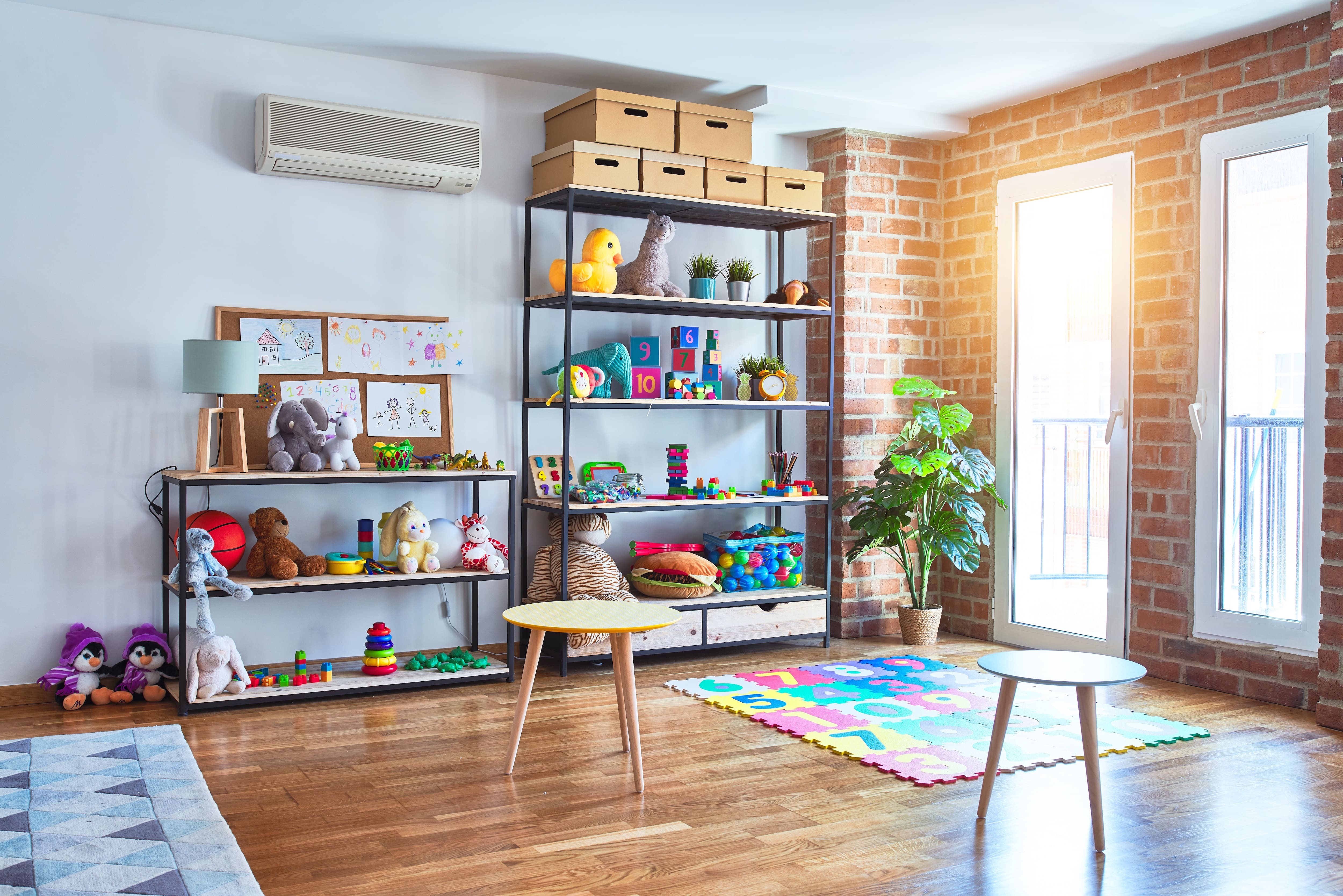 A bright open playroom with brick walls, wood floors, and open shelves for toy storage