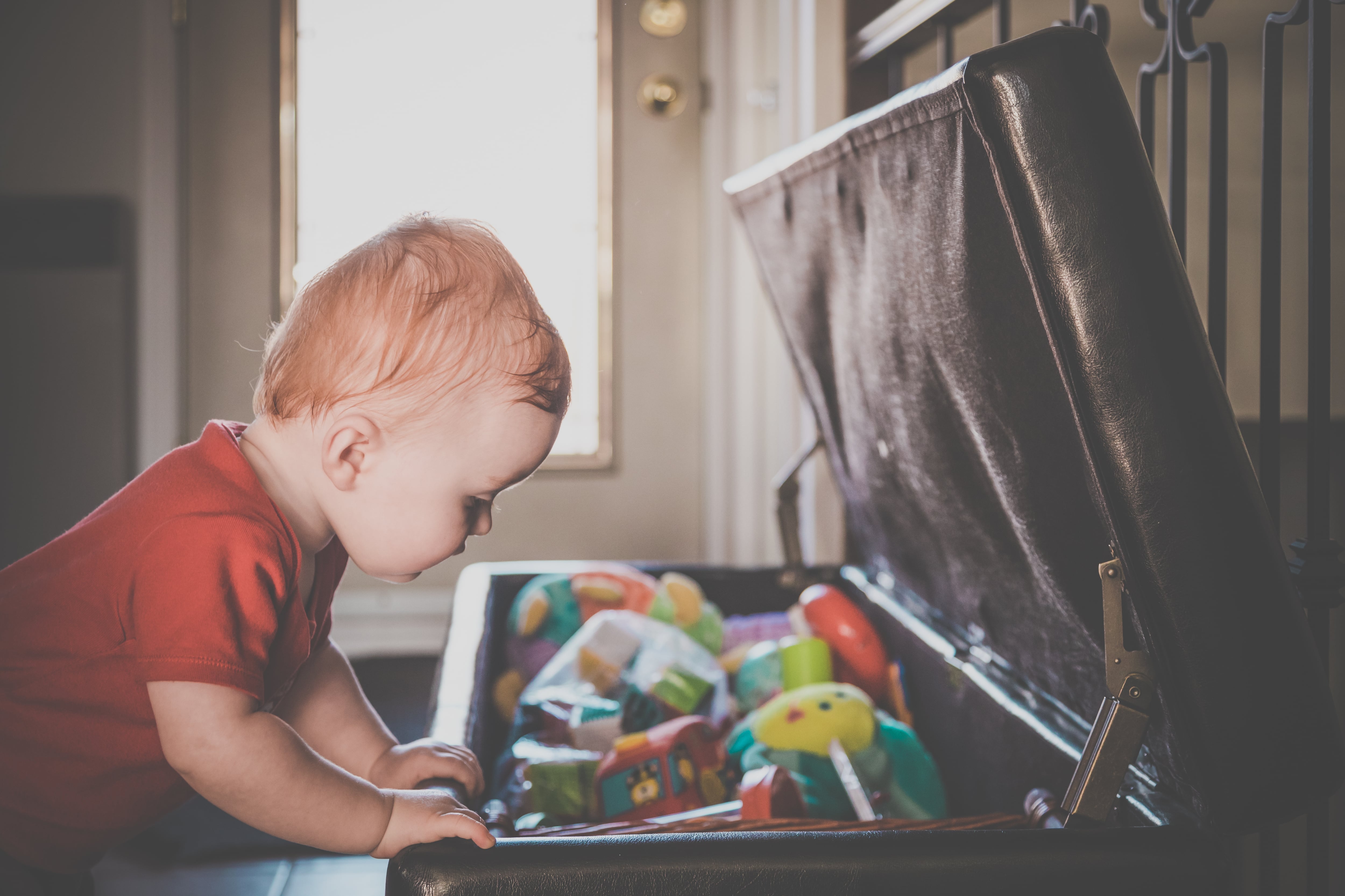 A baby boy looking at toys inside open ottoman storage