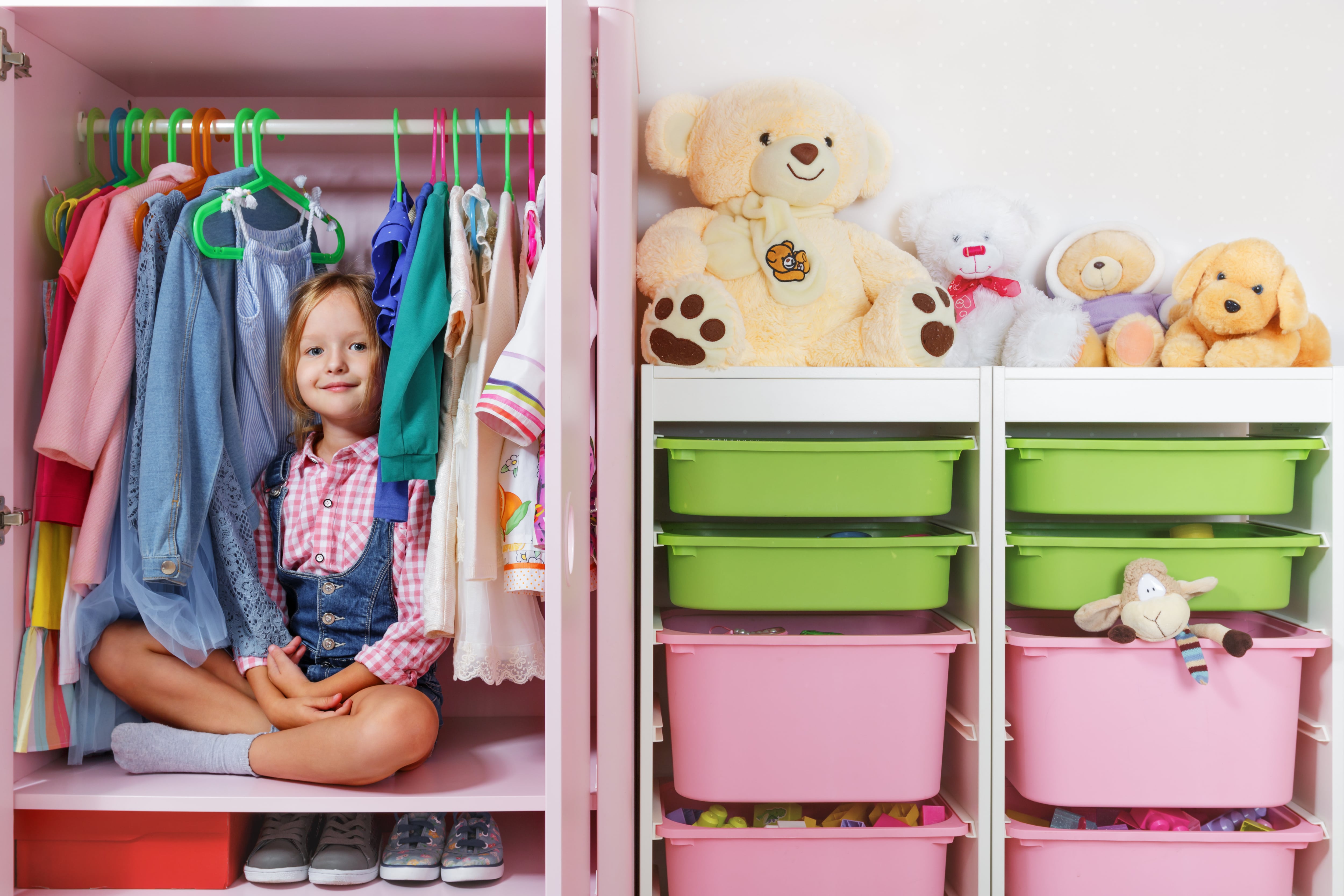 A young girl sitting in a wardrobe unit full of children’s clothes and toys