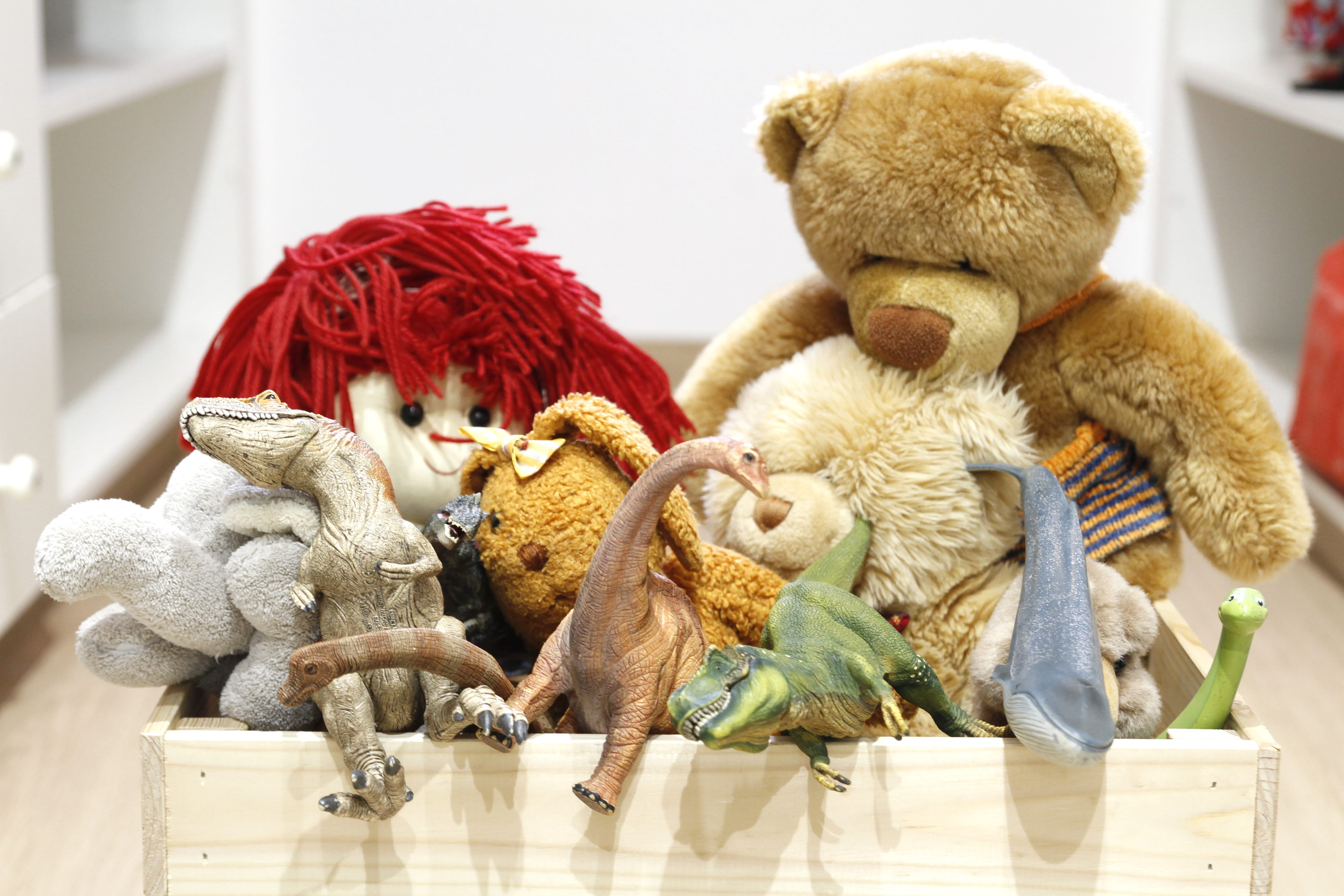 A pinewood crate overflowing with stuffed animals and plastic dinosaurs