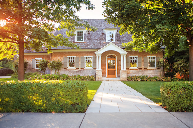 a two story traditional house with brick siding, stone walkway and hedge bushes