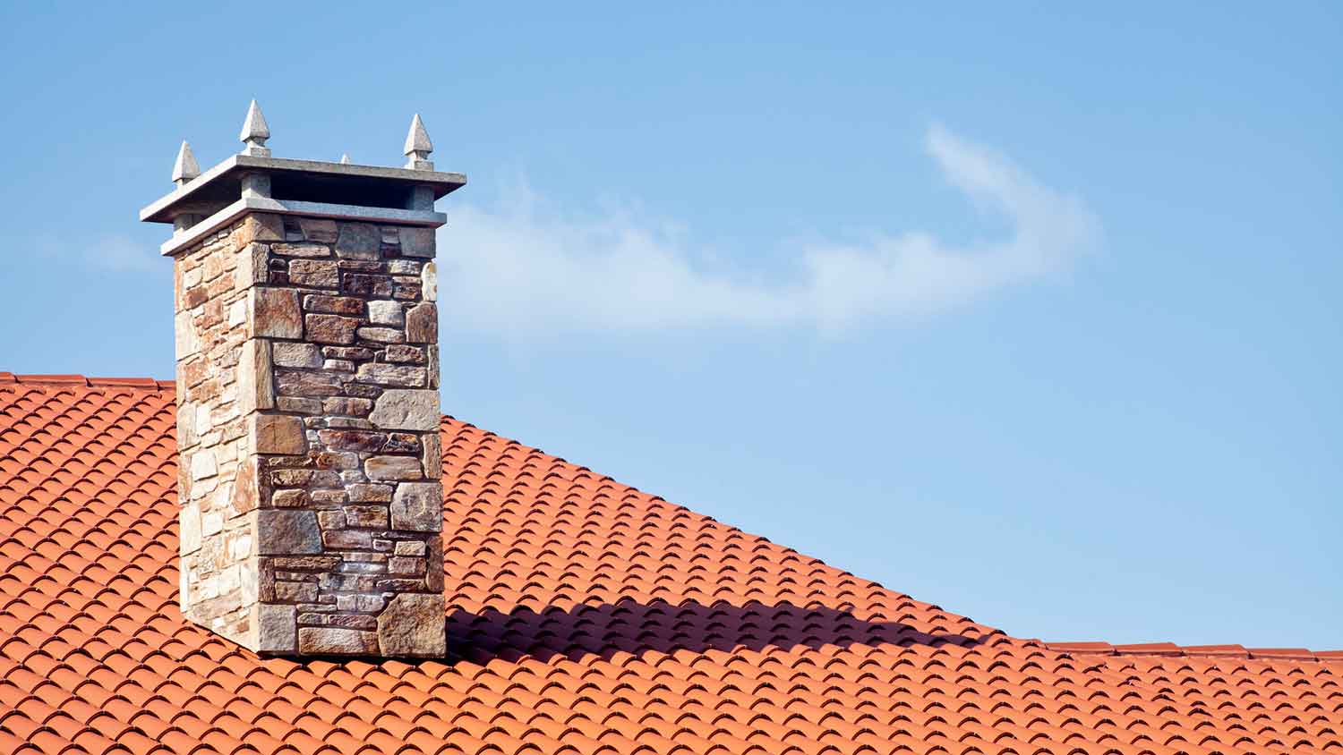 Stone chimney installed in a house with red roof tiles