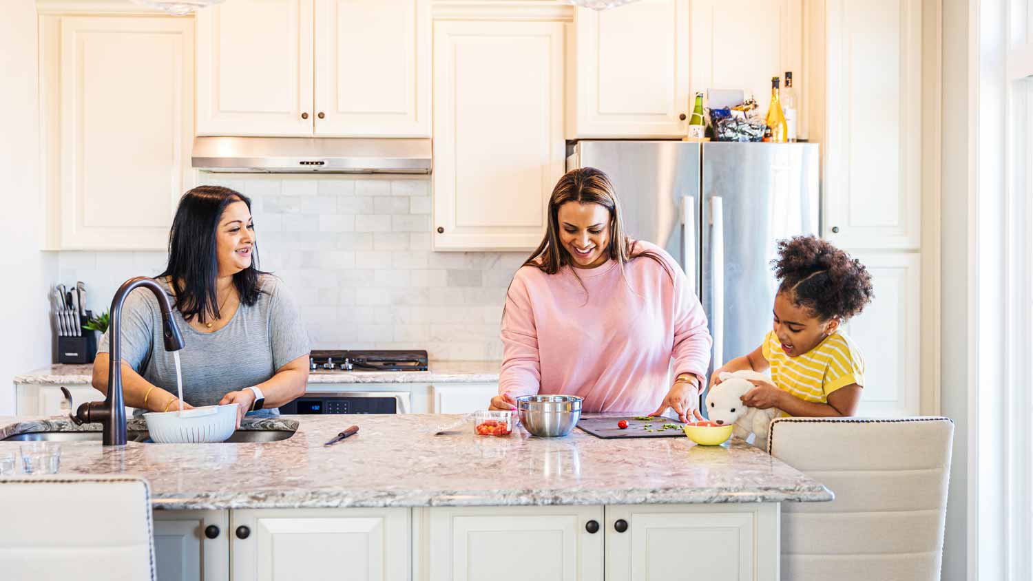 Two women and a kid sitting at a kitchen island with a sink